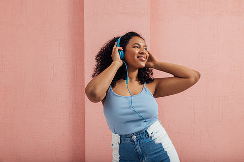 Smiling woman in casuals standing against pink wall listening to