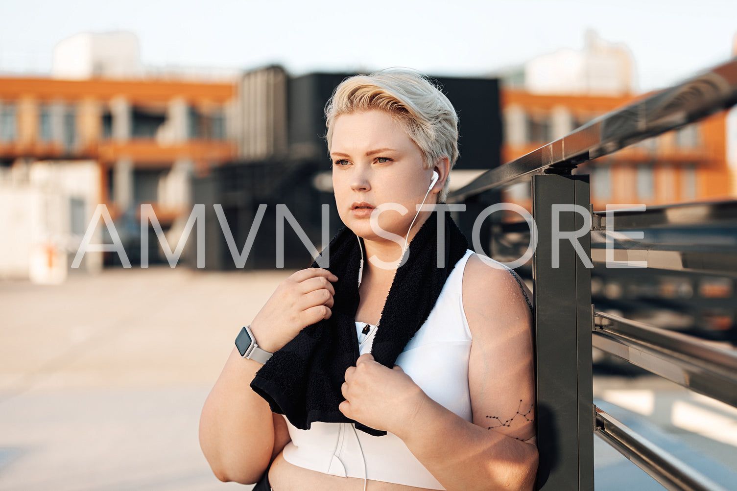 Plus size woman leaning railing on roof. Curvy tired female standing outdoors with a black towel around her neck.	