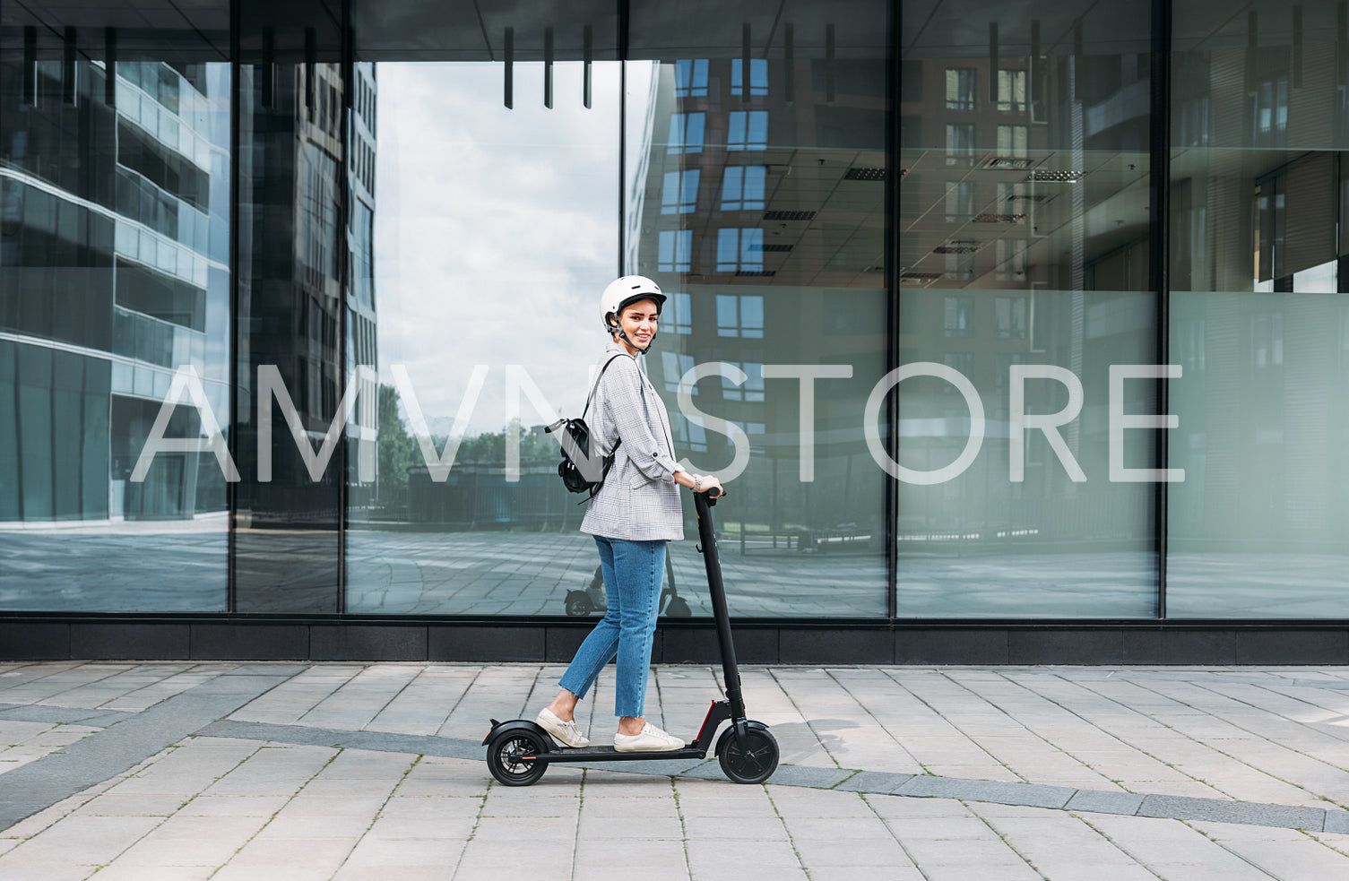 Side view of young smiling businesswoman with cycling helmet on her head driving an electrical push scooter