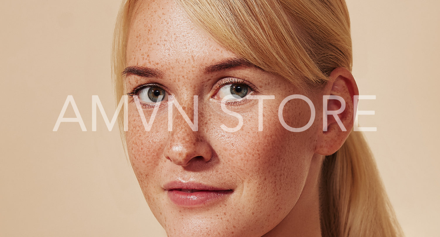 Close-up detailed portrait of a beautiful blond woman with freckled skin. Young female with freckles against a beige backdrop.