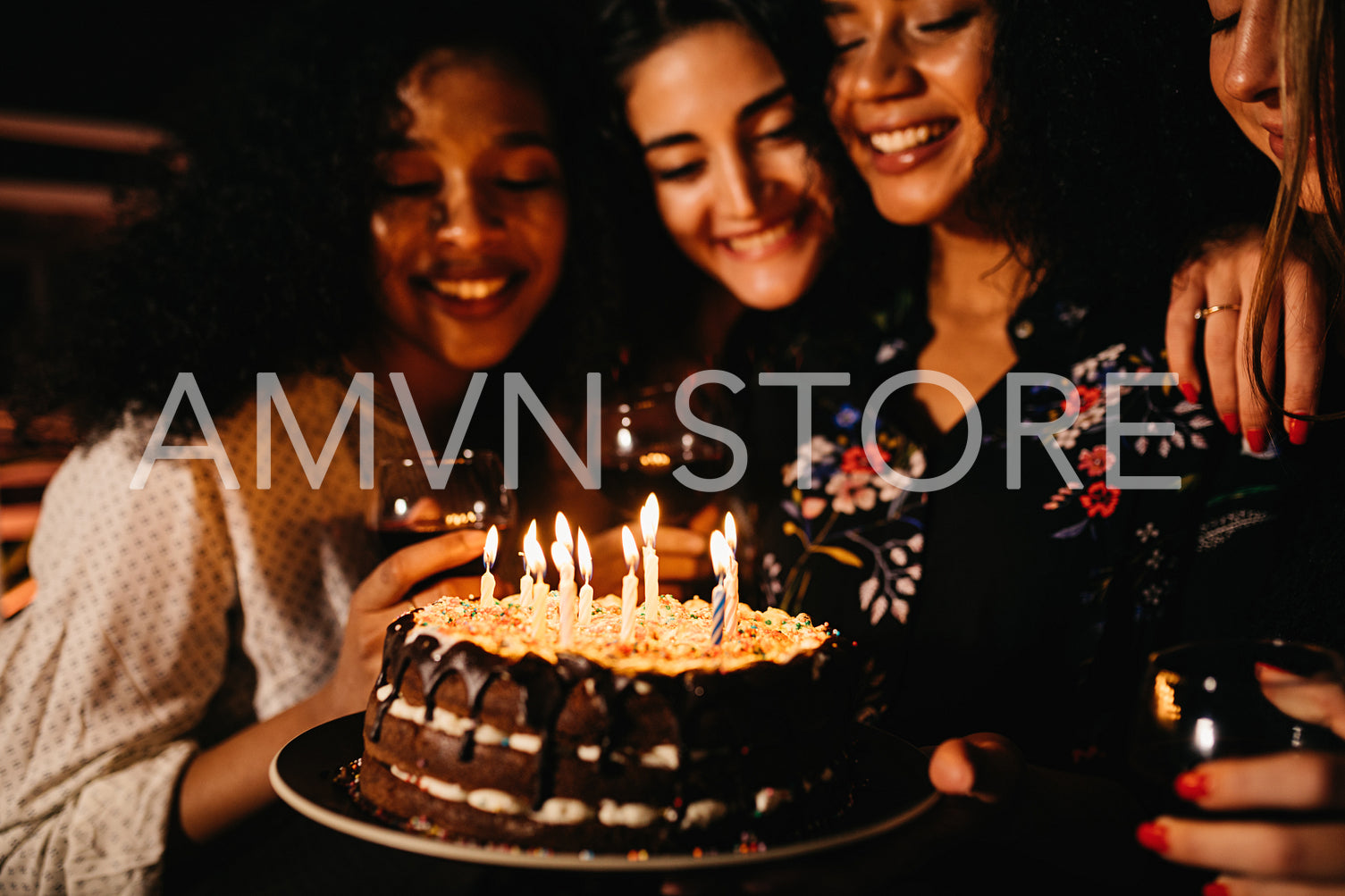 Young woman holding a birthday cake, making wish while friends look on	