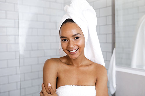 Portrait of an attractive young woman in her bathroom at home, wrapped a towel around head