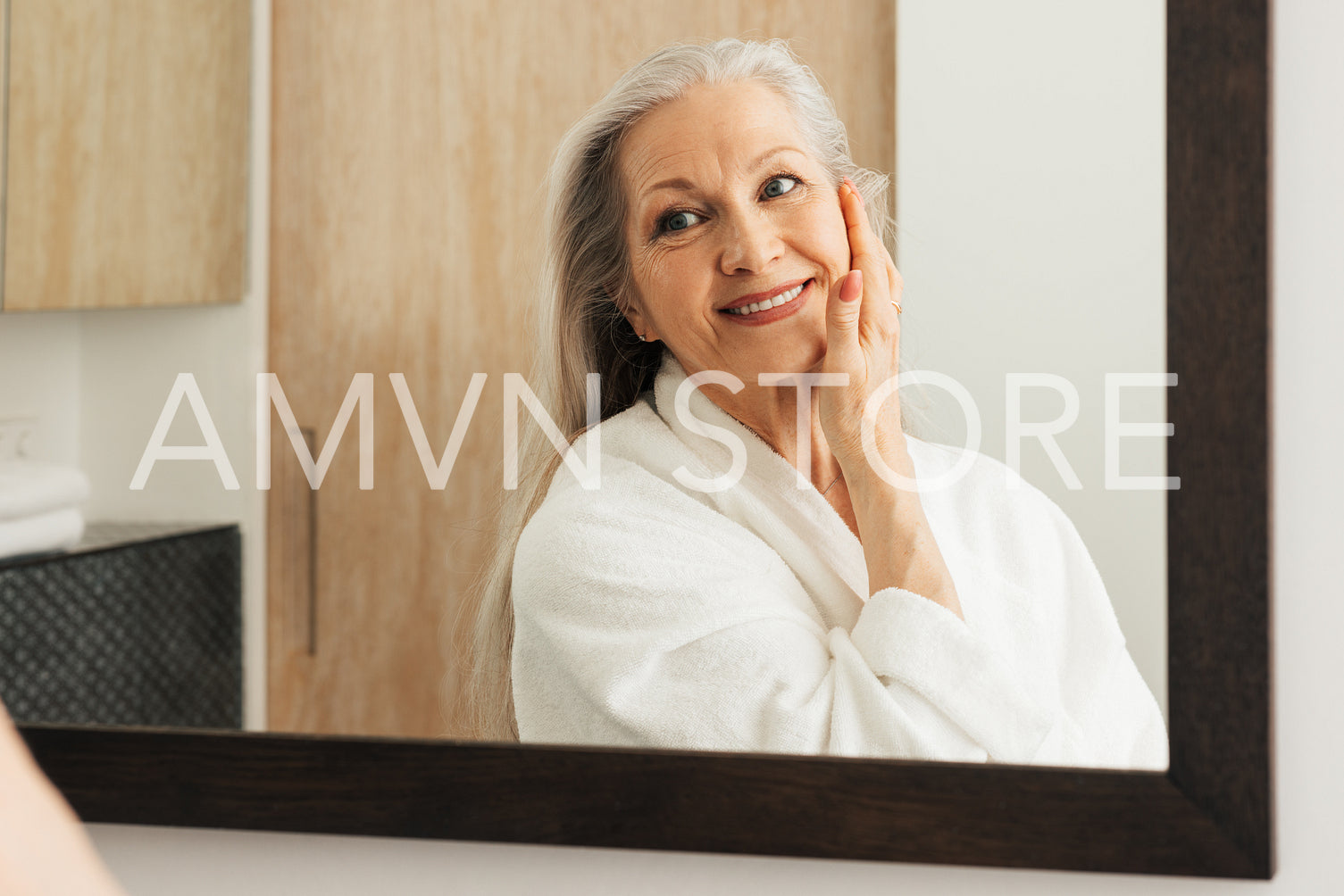 Senior woman with long grey hair touching her face with hand and looking at mirror