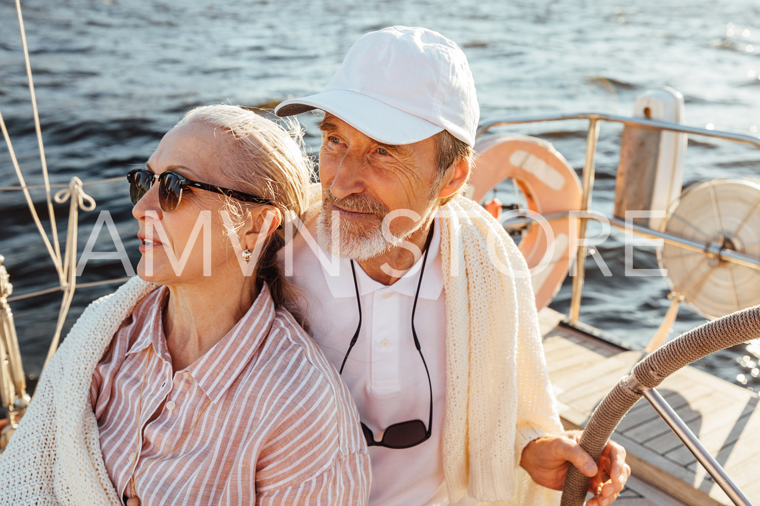 Mature couple wrapped in plaid on yacht. Senior male holding a steering wheel and sitting with his wife on yacht.	