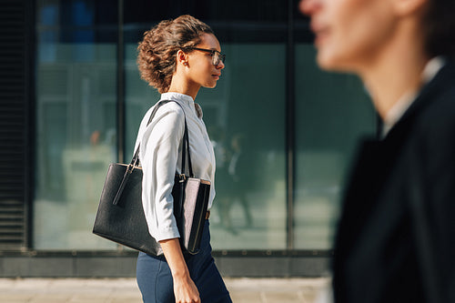 Side view of businesswoman walking outdoors carrying a bag on a city street