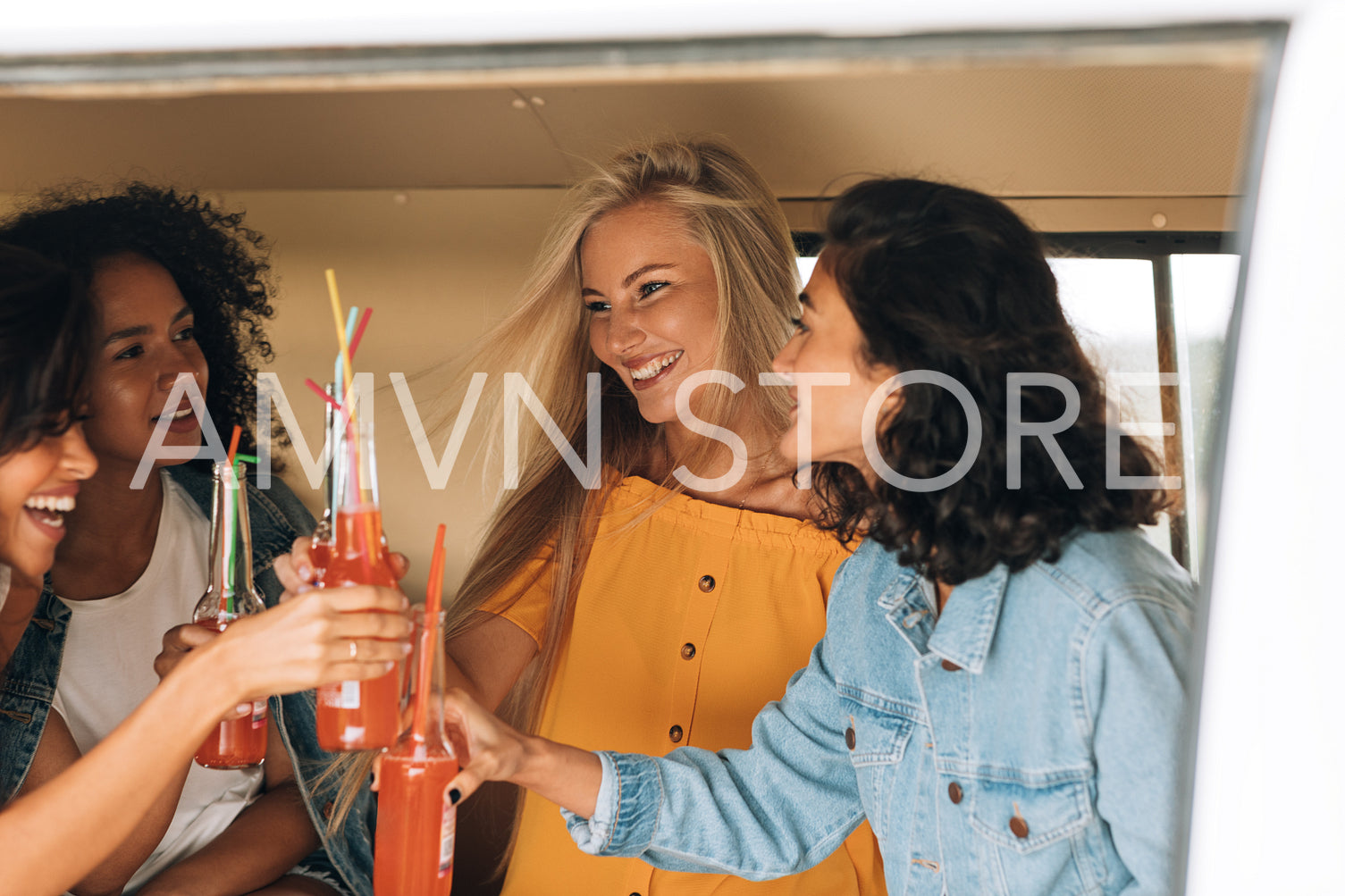 Four women toasting with bottles while sitting in camper van