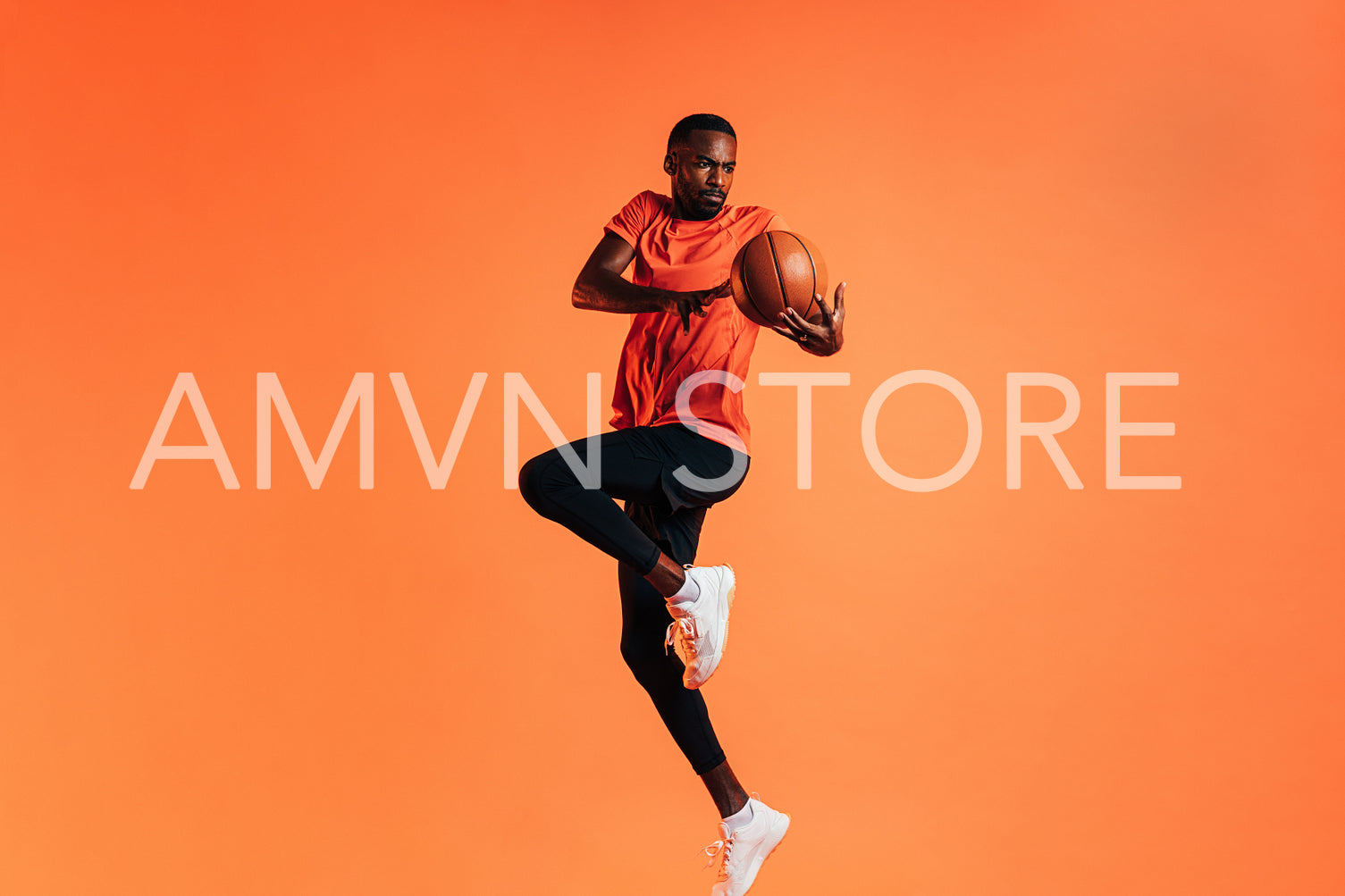 Sportsman jumping in studio against an orange background with basket ball