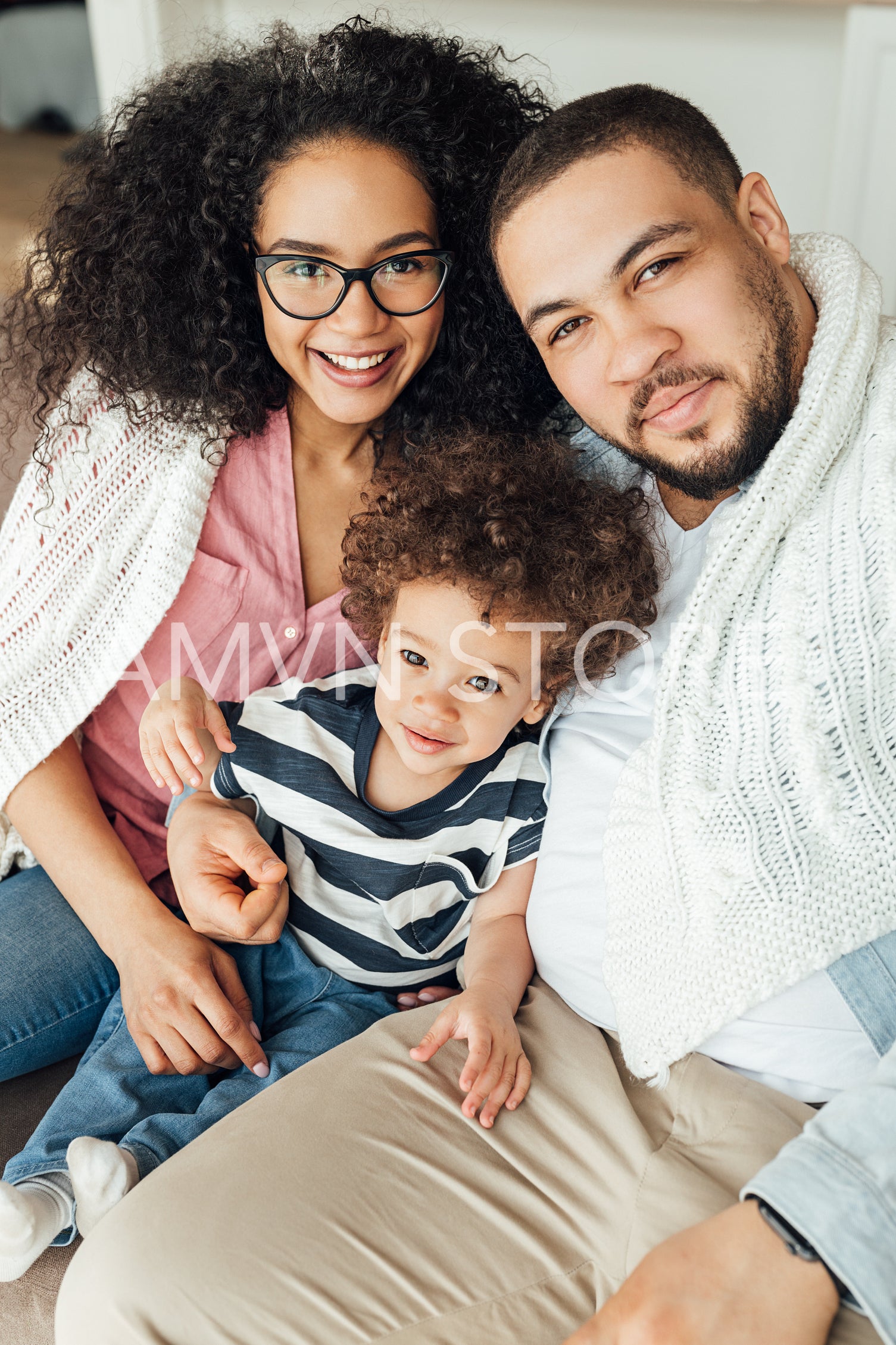 Family of three looking at camera. Mother, father, and son sitting on a couch.	