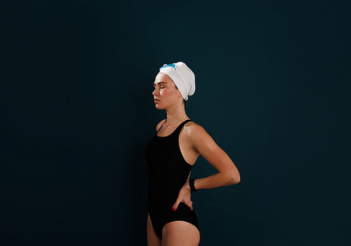 Young female swimmer with closed eyes and hands on hips relaxing over blue background