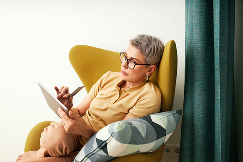 Mature woman in casuals paying by credit card while online shopping from home