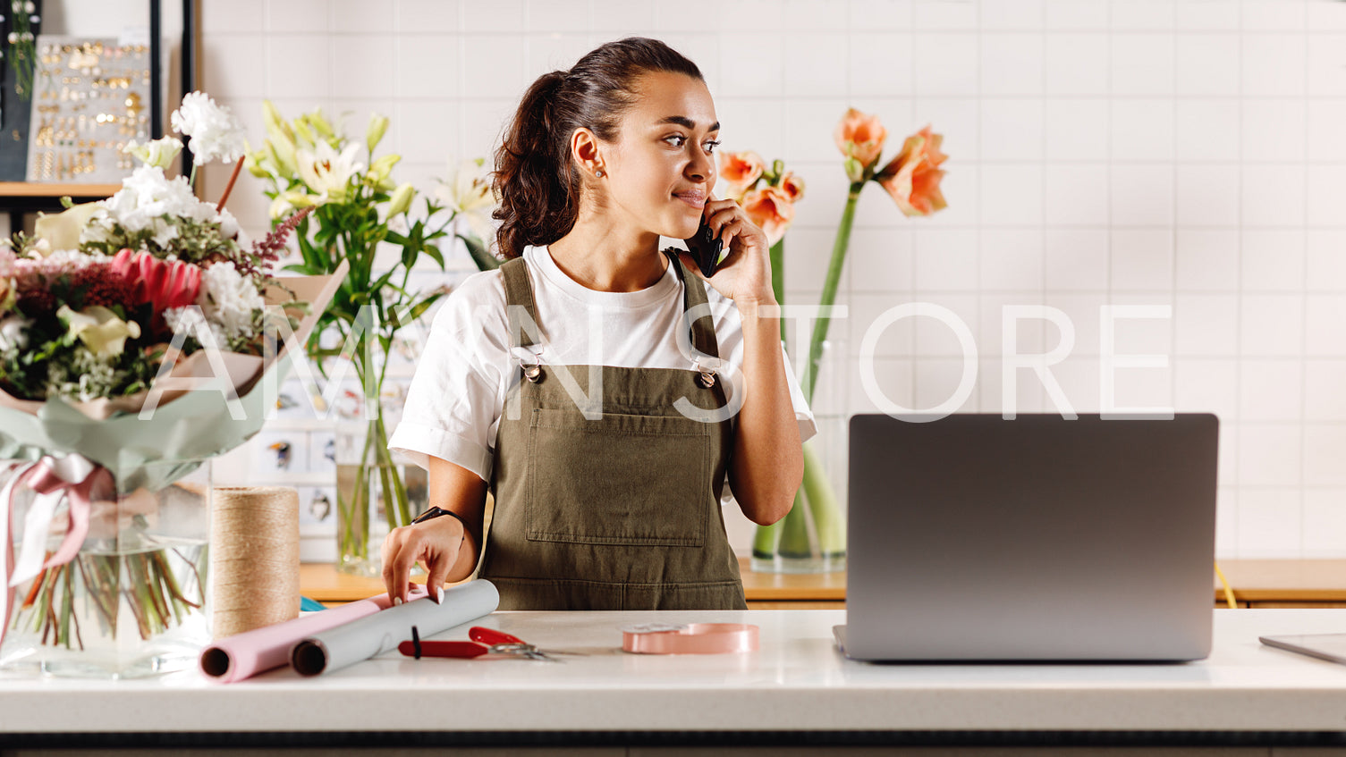 Flower shop owner talking on cell phone at counter looking away	