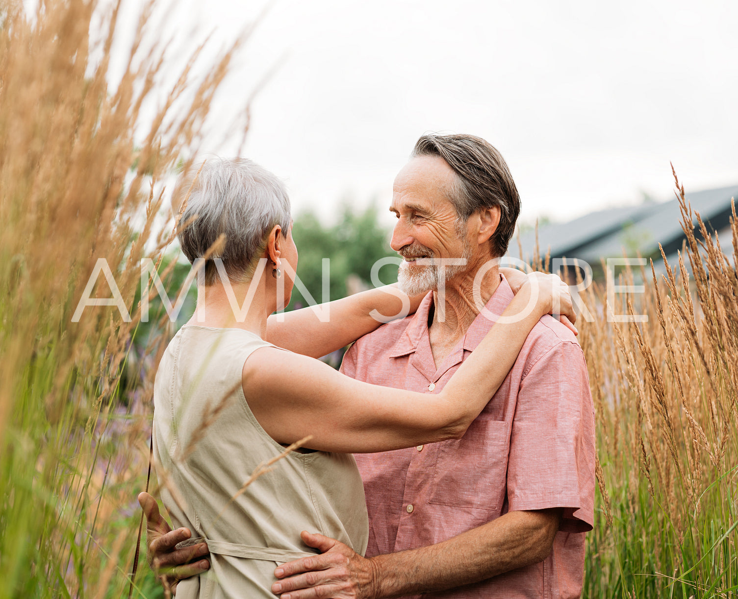 Smiling mature man with grey hair hugging her wife. Senior couple standing on a wheat field.