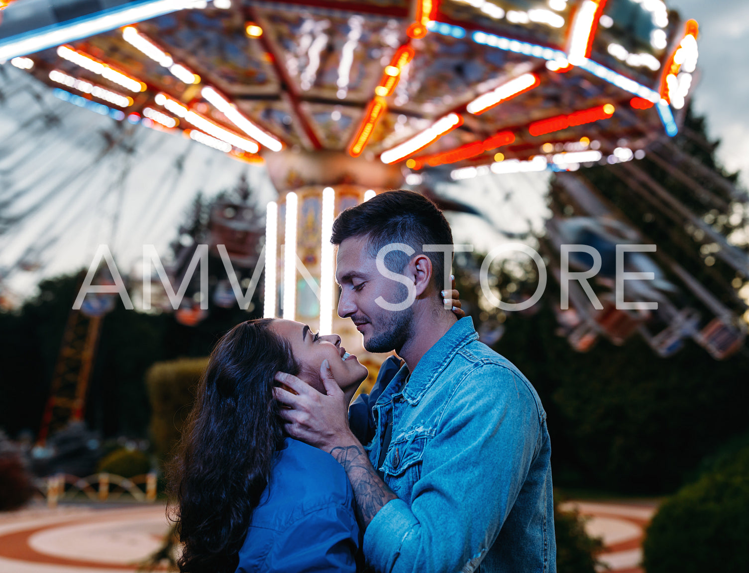 Happy couple in an amusement park. Young couple in love hugging and looking at each other against the carousel.