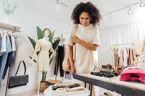 Young woman in stylish clothes standing at a table with accessories in a clothing shop