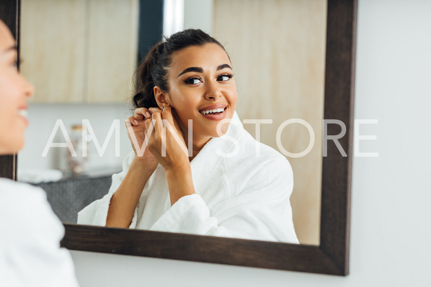 Beautiful smiling woman putting on an earring looking at a mirror in bathroom	