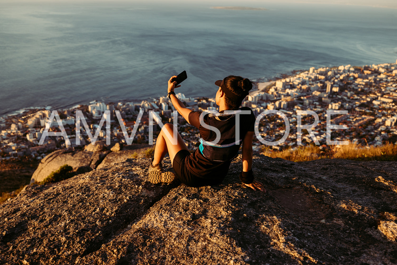 Rear view of female trail runner relaxing on the top of the mountain at sunset