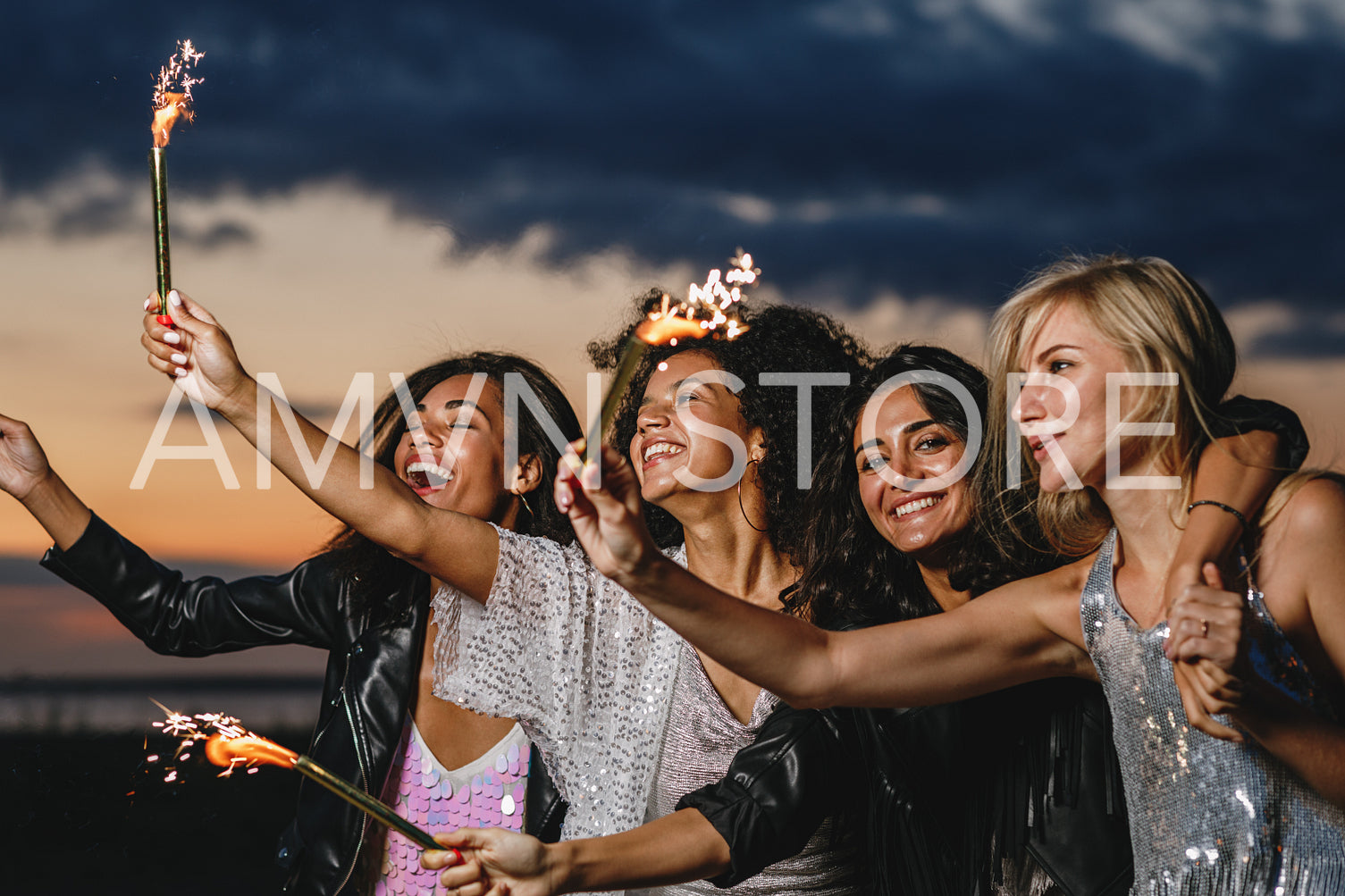 Happy friends with sparklers at sunset. Four laughing friends celebrating with fireworks outdoors.	