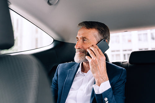 Mature businessman sitting on the backseat in the car. Senior man talking on the cell phone in a taxi.