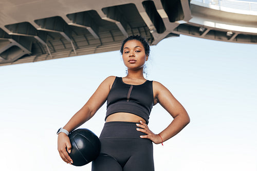 Low angle shot of a confident sportswoman with medicine ball standing outdoors under a bridge