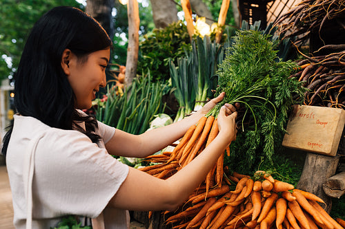 Woman buying carrot on the farmers market. Young female holding a bunch of carrots.