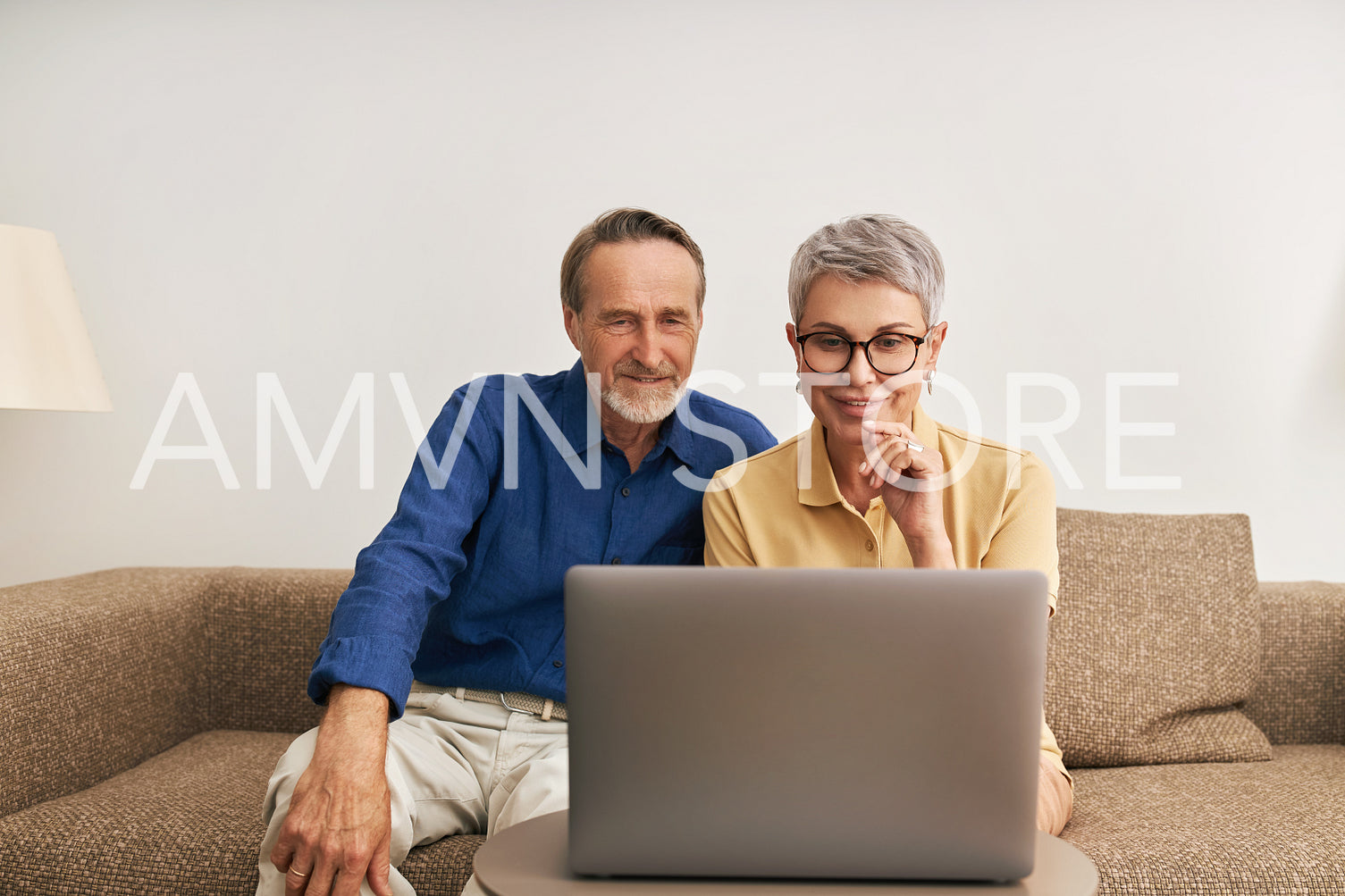 Elderly couple sitting in front of a laptop in a living room communicating during a video call	