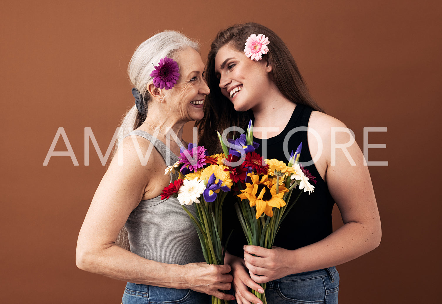 Two women of different ages with bouquets and flowers in their hair looking at each other