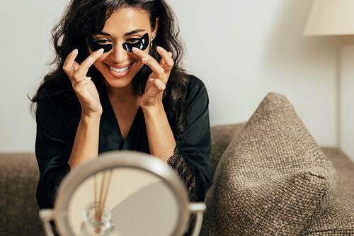 Brunette woman looking at the mirror applying black eye patches with fingers