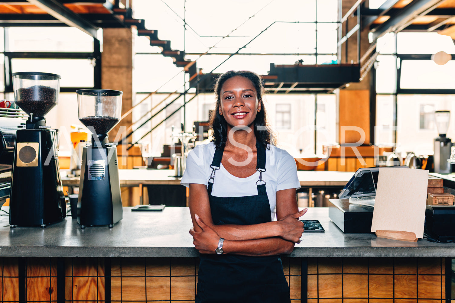 Portrait of a smiling coffee shop owner standing at counter wearing apron and arms crossed	