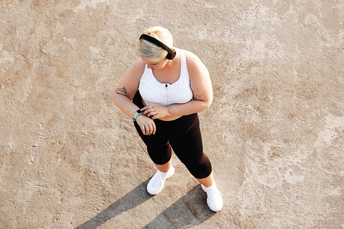 Shot from above of a young woman with plus size body checking activity tracker