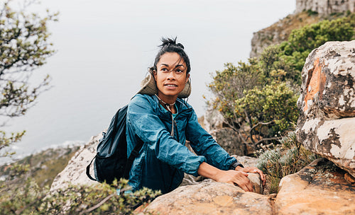 Portrait of a young woman relaxing while hiking on a mountain. Female in sports clothes climbing up.