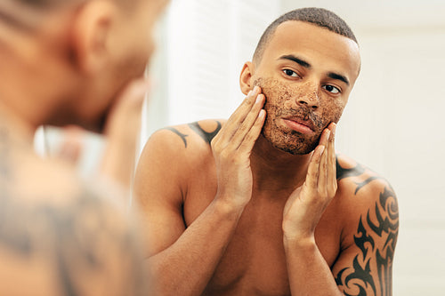 Handsome man applying natural scrub in front of a mirror