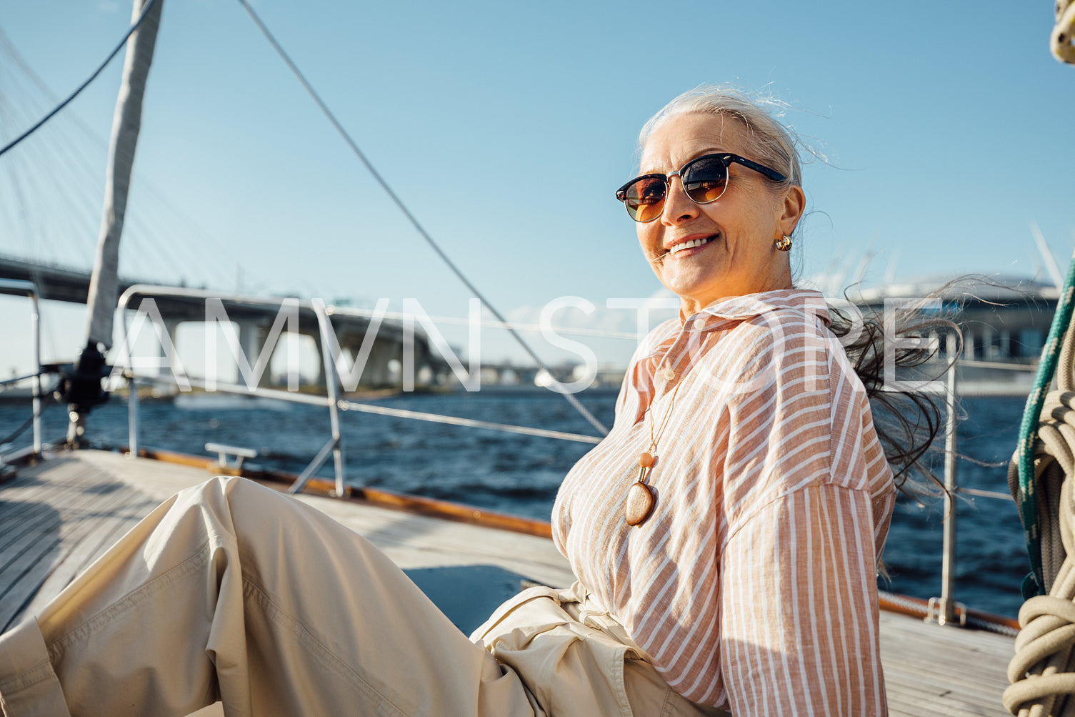 Elegant mature woman wearing eyeglasses on a private yacht and looking straight at a camera. Smiling female sitting on a sailboat and enjoying a vacation.	