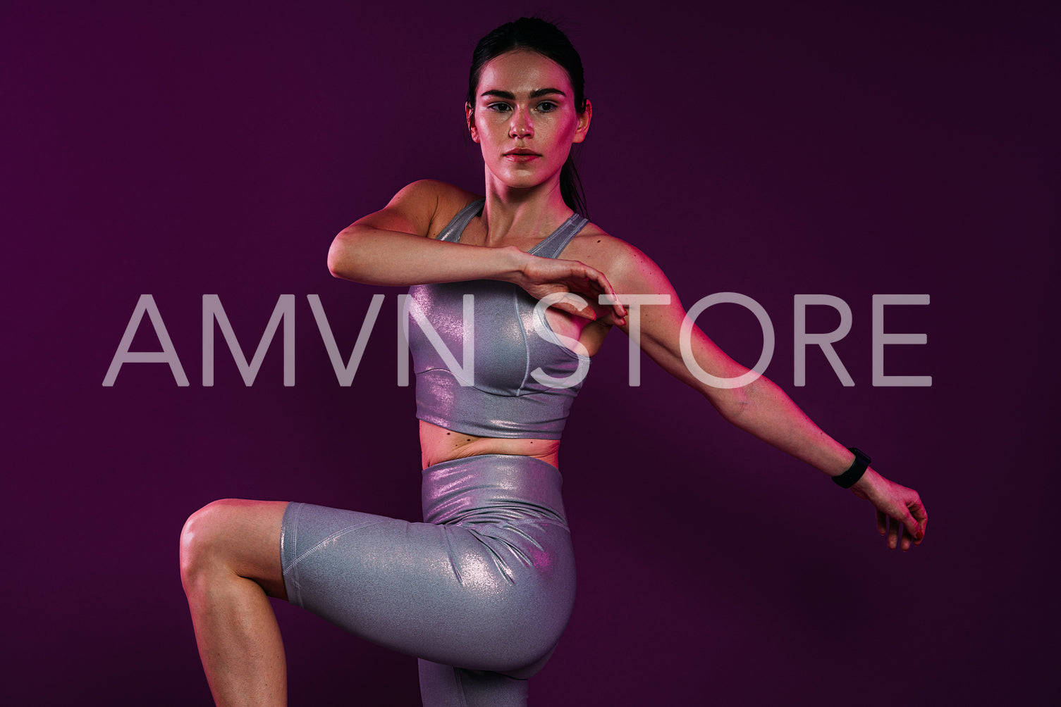 Woman in silver fitness attire doing warming-up exercises over a magenta backdrop