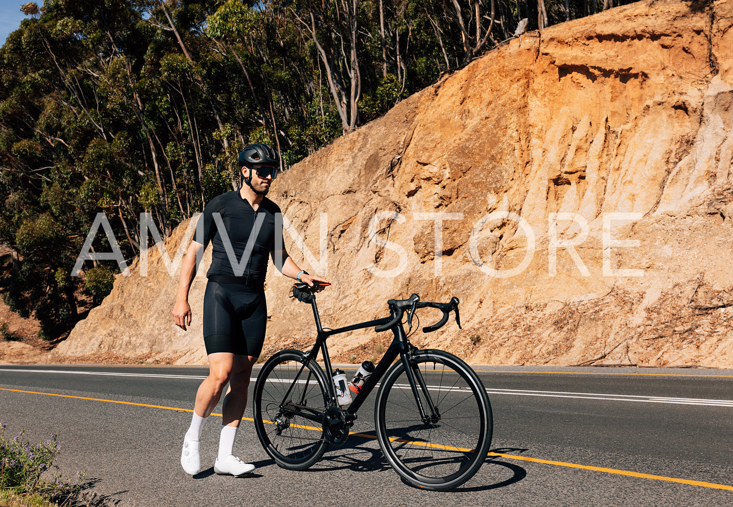 Young male cyclist holding his bicycle by a saddle walking on an empty road