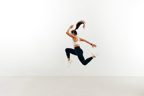 Side view of woman with muscular body jumping against white wall