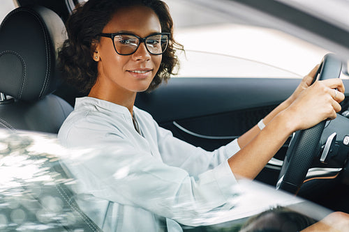 Young woman driving a car. Smiling female looking at camera while sitting on driver seat.