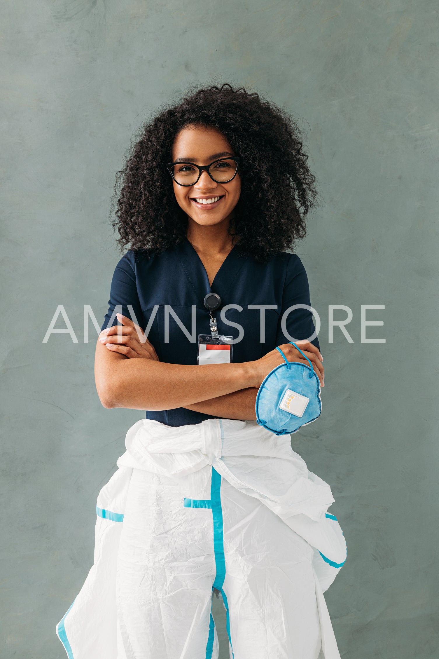 Young medical specialist in eyeglasses holding a mask, wearing a protective suit and uniform	