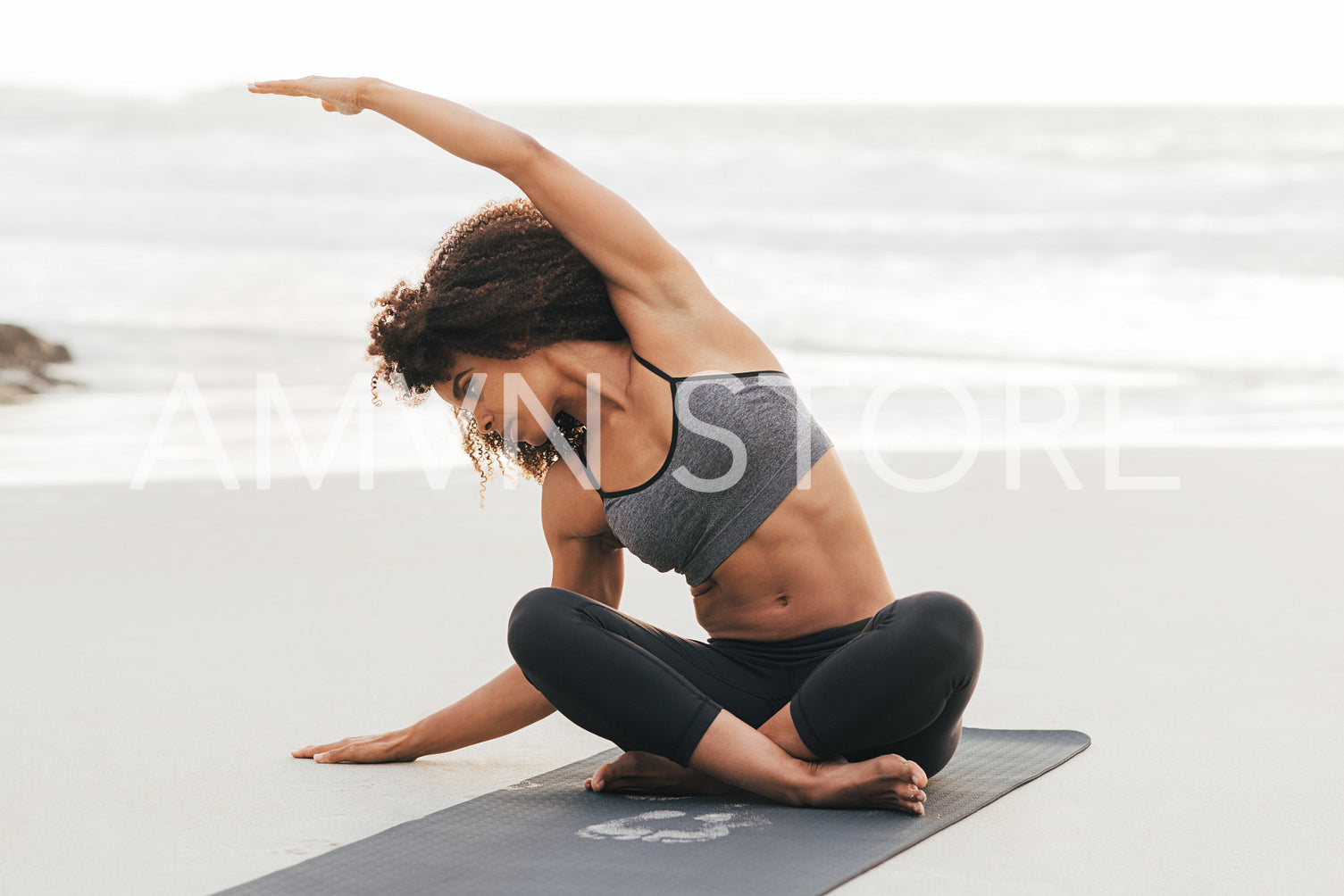 Woman in sportswear doing flexibility exercises while sitting on a mat on a beach