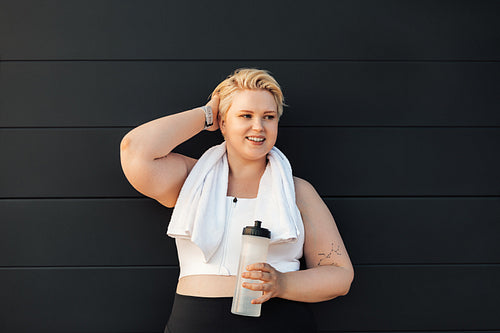 Smiling plus size woman standing at wall. Positive woman relaxing after training