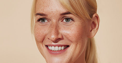 High-detailed close-up portrait of a smiling woman with freckles. Young cheerful female with blond hair over pastel backdrop.