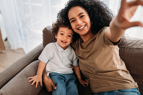 Young woman and her little son taking selfie. Happy mother with her kid sitting on a sofa.