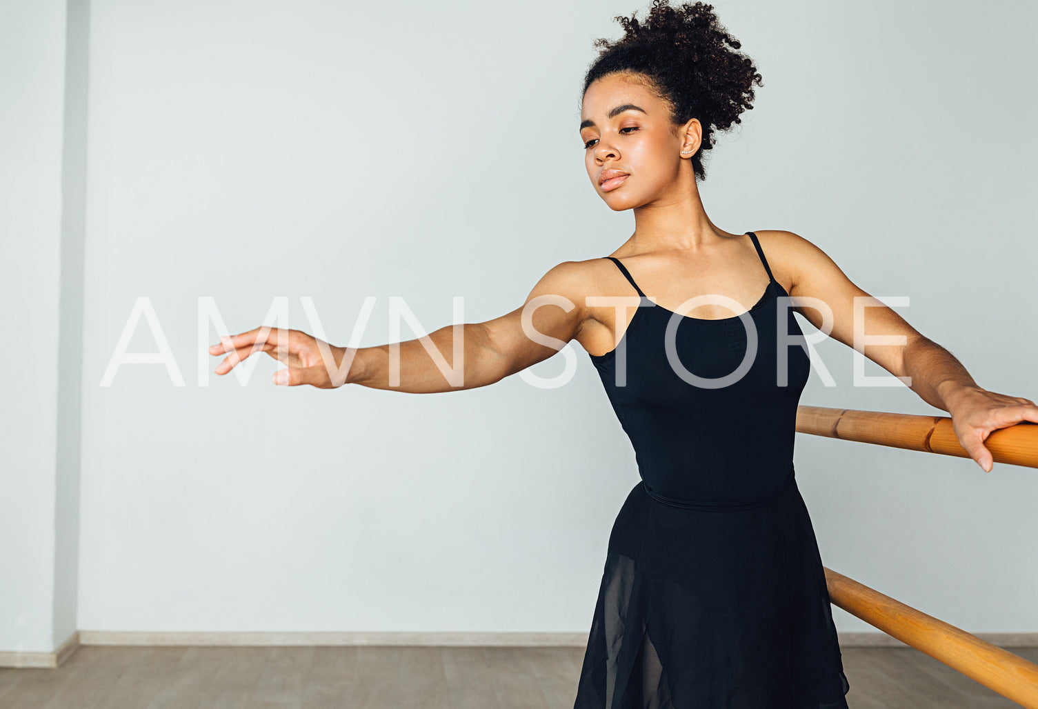 Young African American woman practicing ballet exercises holding a wooden handrail	