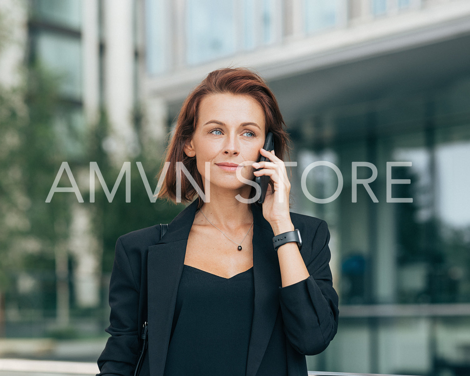 Middle-aged businesswoman in formal clothes making phone call. Portrait of a young adult female with ginger hair talking on a mobile phone while standing outdoors.