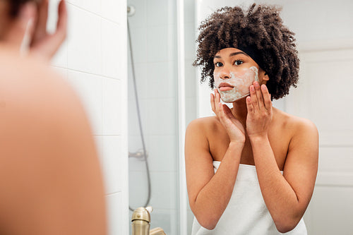 Young woman standing in front of a mirror wrapped in white towel