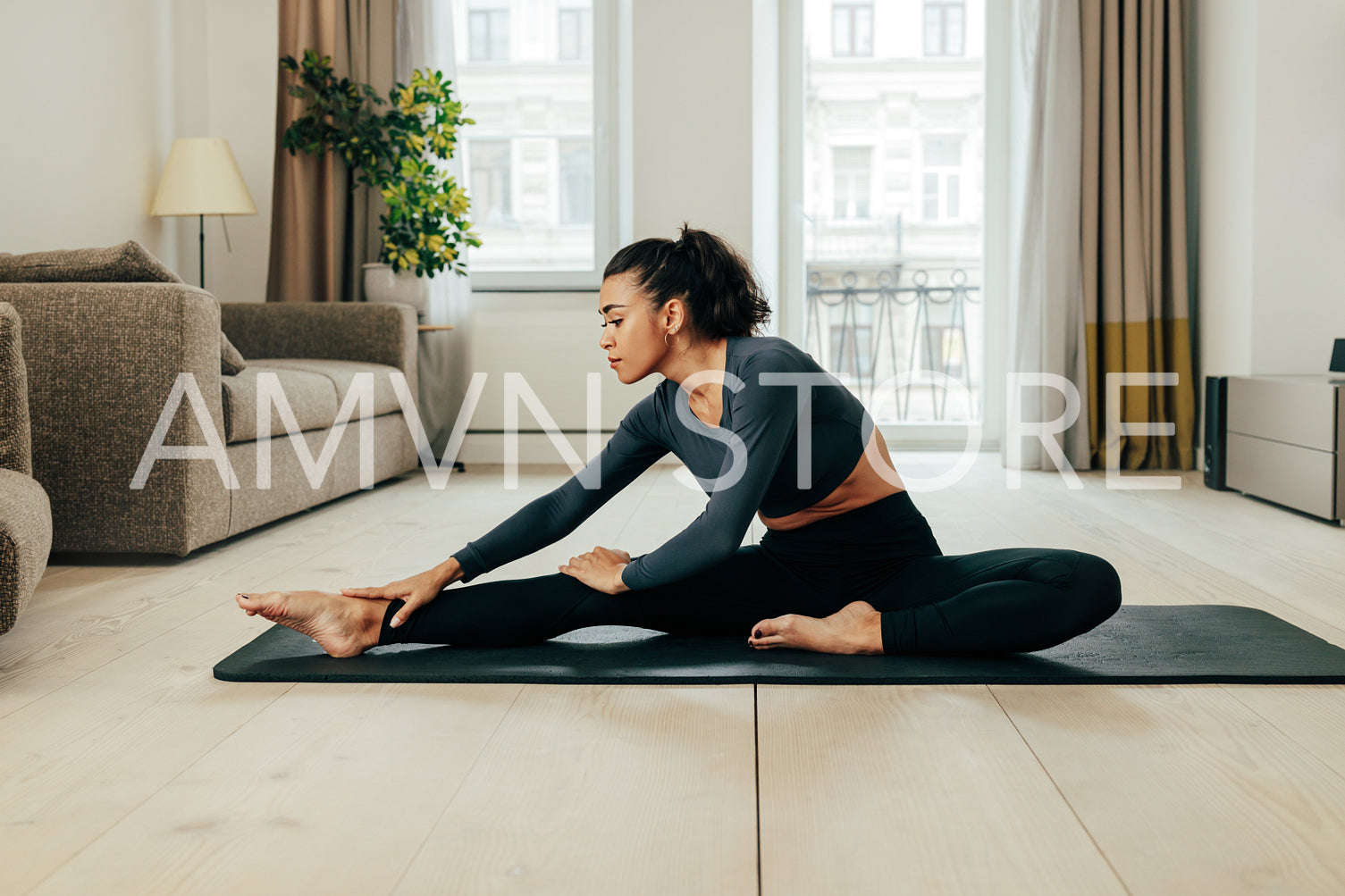 Side view of a young woman in sport clothes warming up her leg on mat at home	