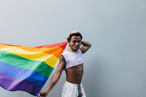 Young man with rainbow flag looking at camera outdoors