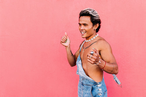 Young happy guy dancing against pink wall and looking away