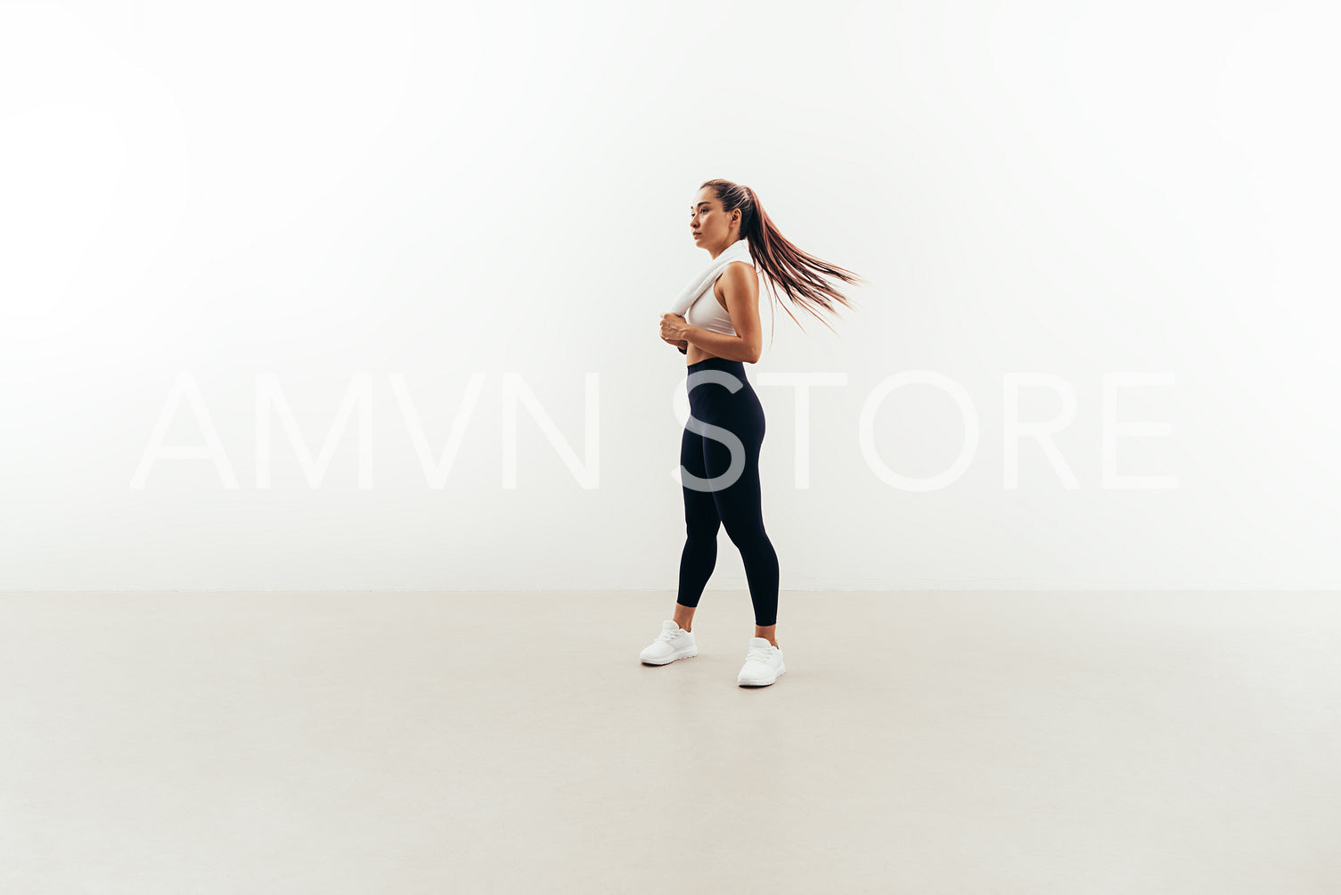 Young fit woman with white towel on her neck relaxing after workout indoors