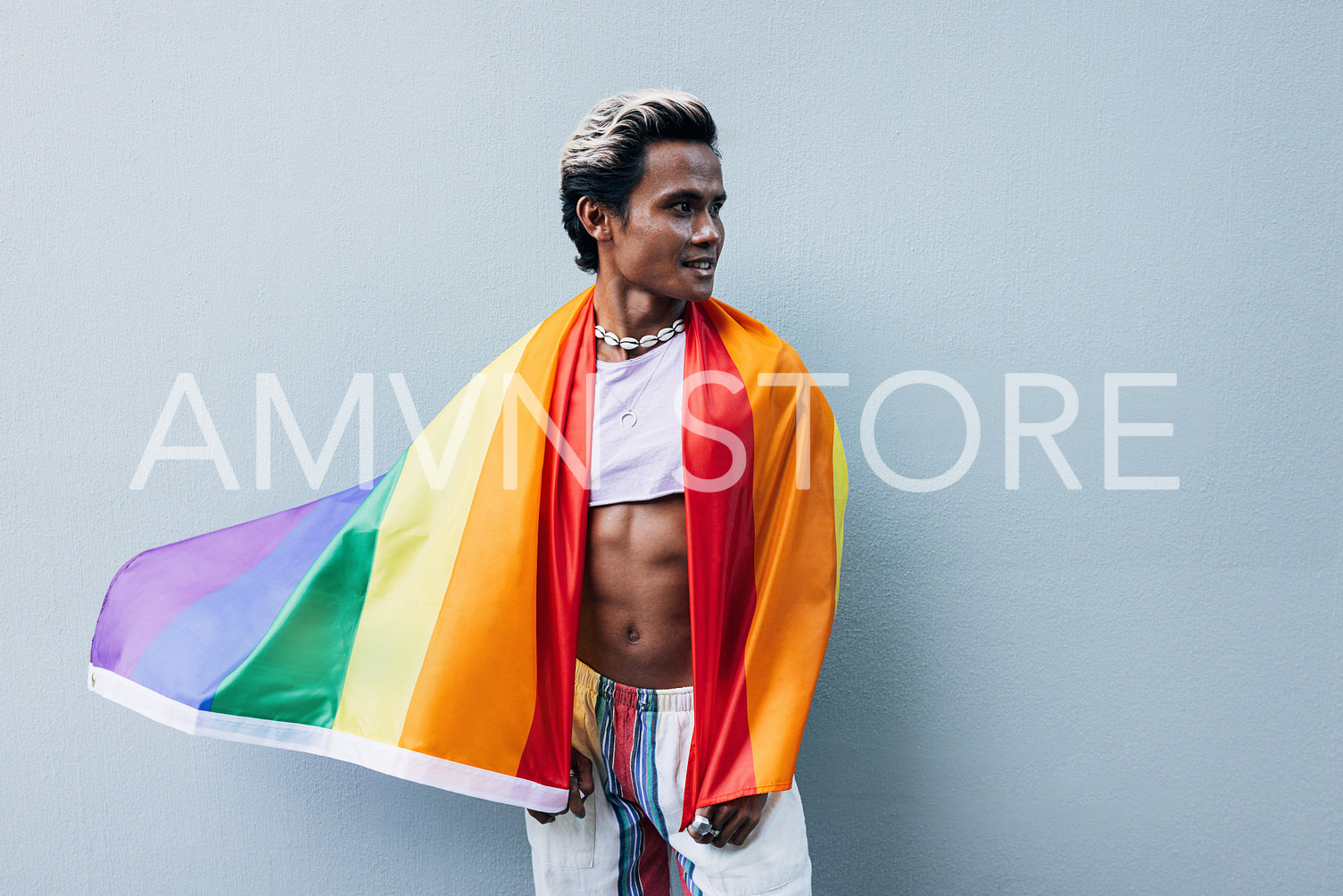 Handsome muscular man posing against grey wall with rainbow flag