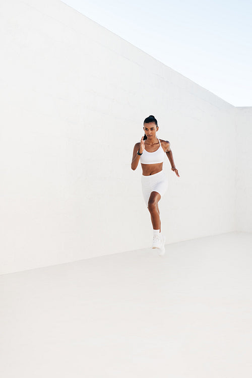 Full length of a slim female sprinting against a white wall. Young athlete jogging outdoors.